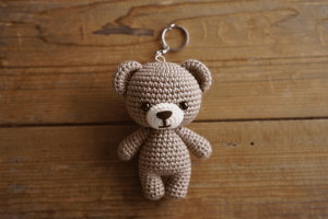 Móc khóa gấu bông handmade dễ thương, được làm bằng len thủ công, đặt trên nền gỗ mang phong cách cozy