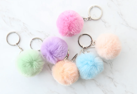 Bộ sưu tập móc khóa cục bông với nhiều hình dạng và màu pastel dịu dàng, sắp xếp trên nền vải trắng tinh tế.